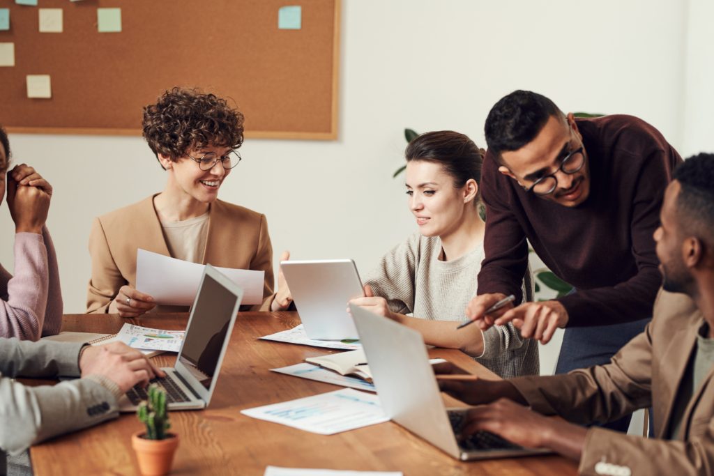 Group of six people sat around a table at a business meeting with laptops