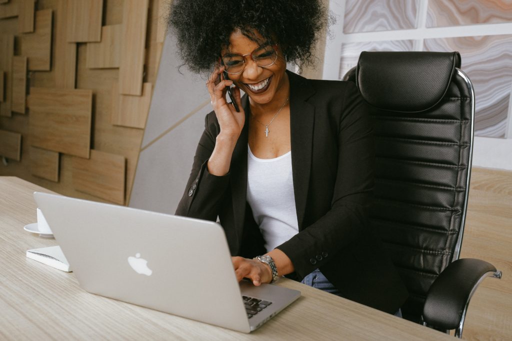 Woman sitting at desk with laptop in front of her with mobile phone to ear.