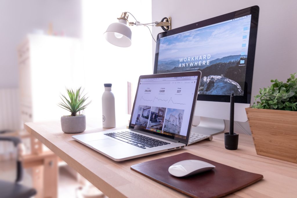 image of silver laptop on a brown, wooden desk infront of a larger black monitor. On the black monitor text reads, "work hard anywhere"