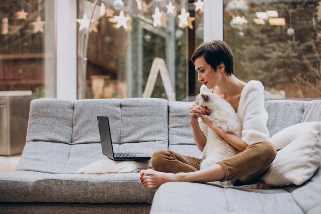 Young woman with cat working on laptop from home