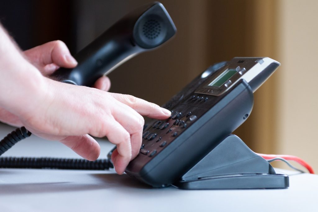 Images features someone holding a phone receiver in their hand, reaching to dial a number on the phone keypad.