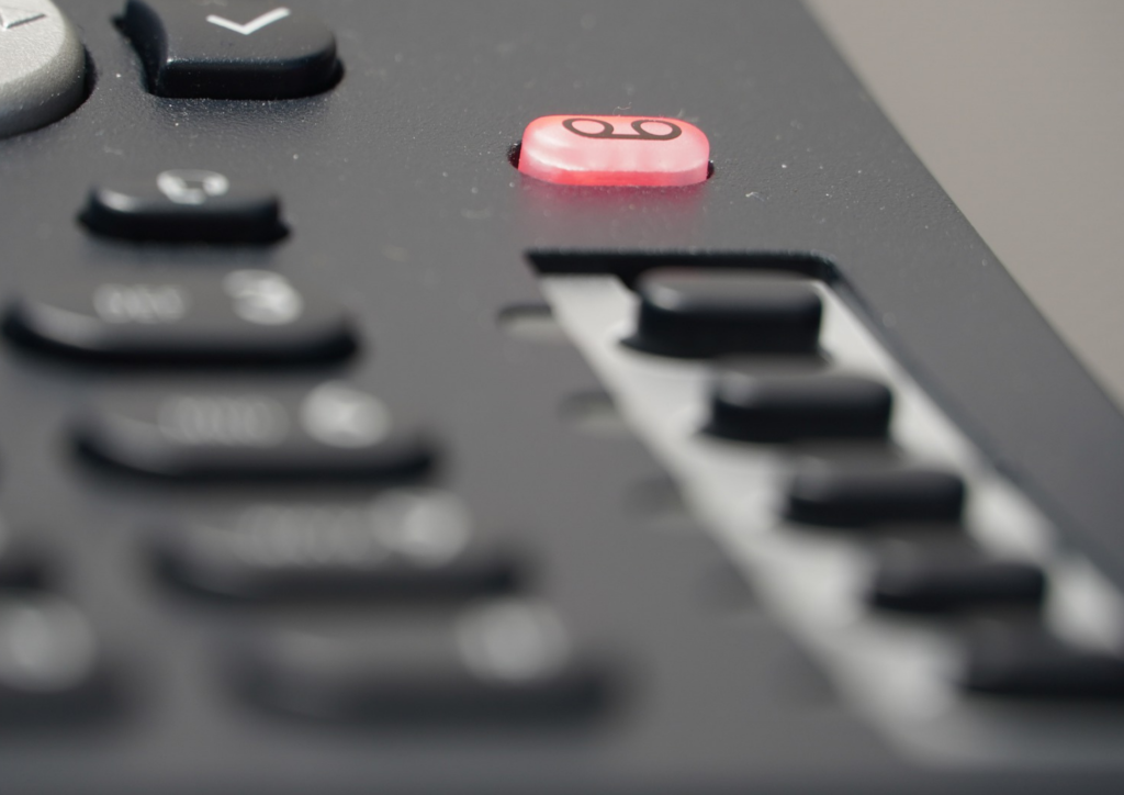 Image features a close-up of a phone keypad, with a red button lit up on the phone. 