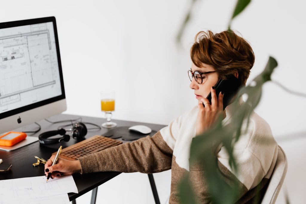 Image shows a lady making handwritten notes whilst making a phone call on her mobile phone.