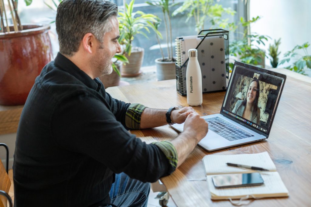 Image of a man working from on a video call on a laptop sat at a wooden desk