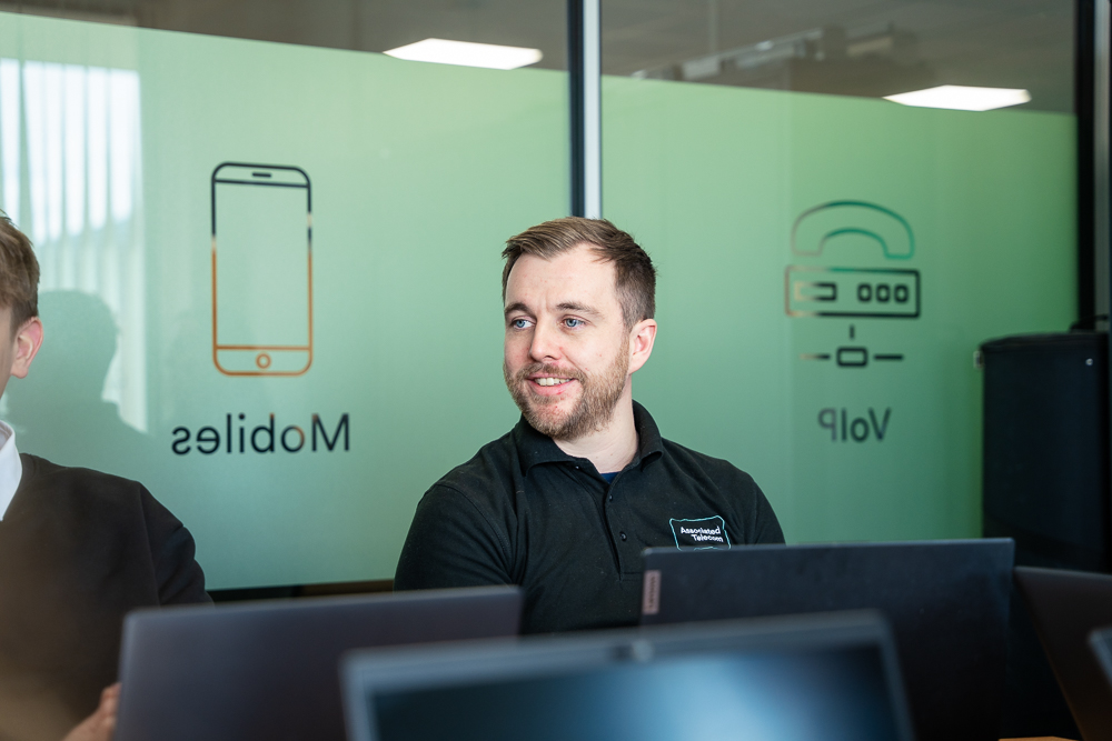 Associated Telecom employee at a laptop in front of branded office signage.