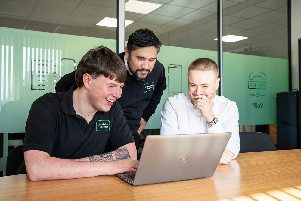 Associated Telecom staff collaborating on laptops in a business meeting room.