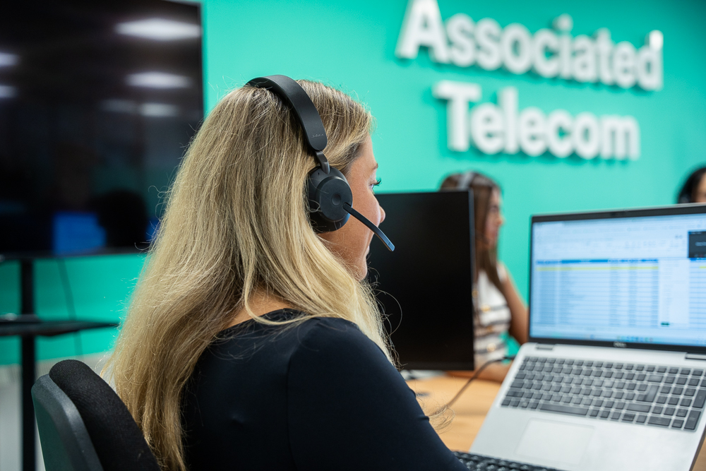 Associated Telecom staff member working at a desk with a headset.