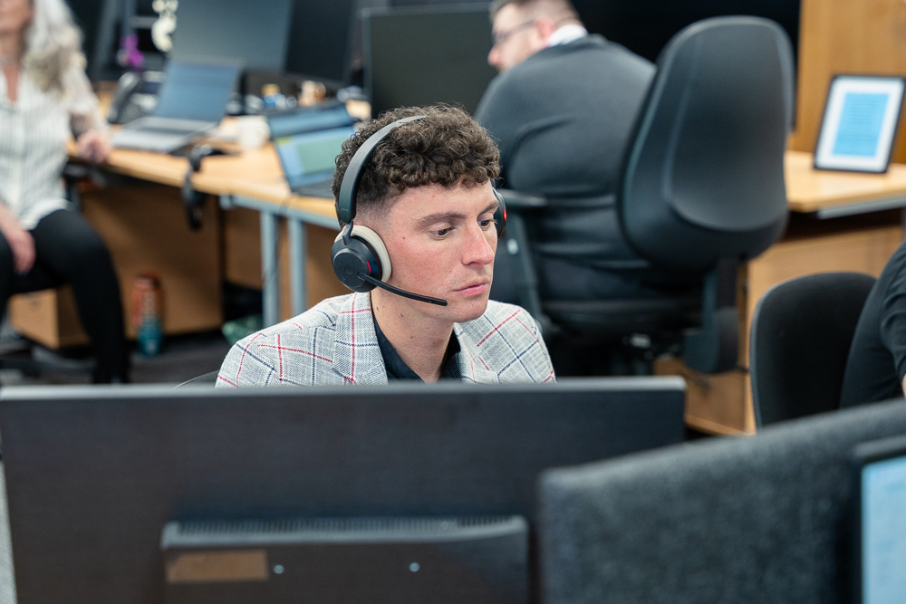 Office worker seated at a computer with a headset on.