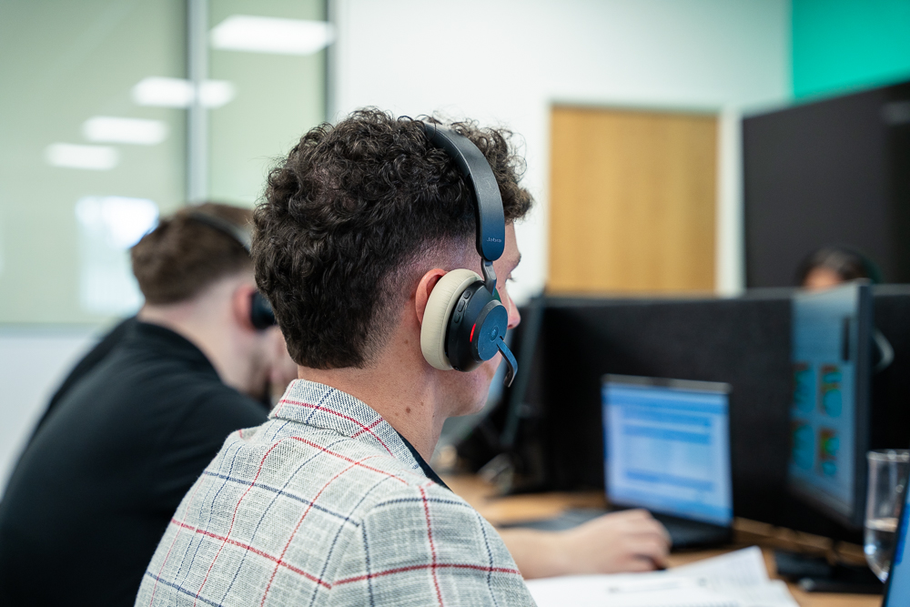 Telecom worker seen from behind using a headset at a desk.