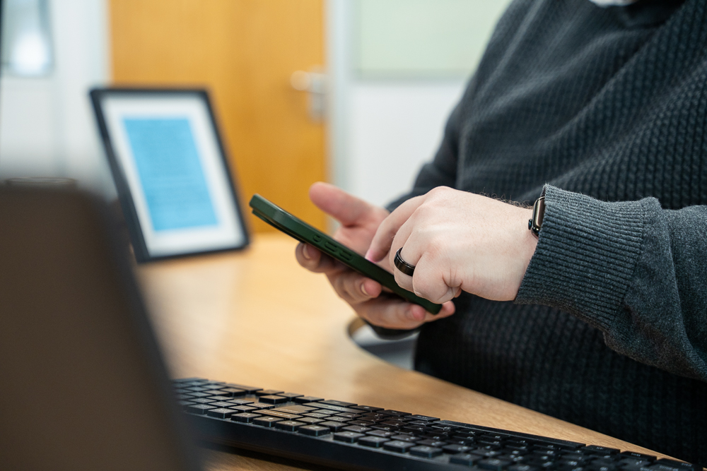 Associated Telecom staff member checking a smartphone at a desk.