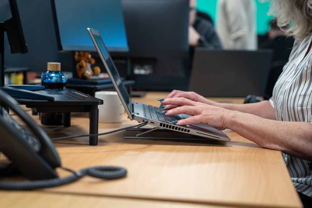 Associated Telecom team member typing on a laptop beside office screens.