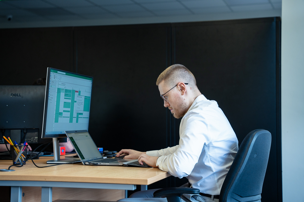 Associated Telecom office worker focused on a laptop and monitor setup.