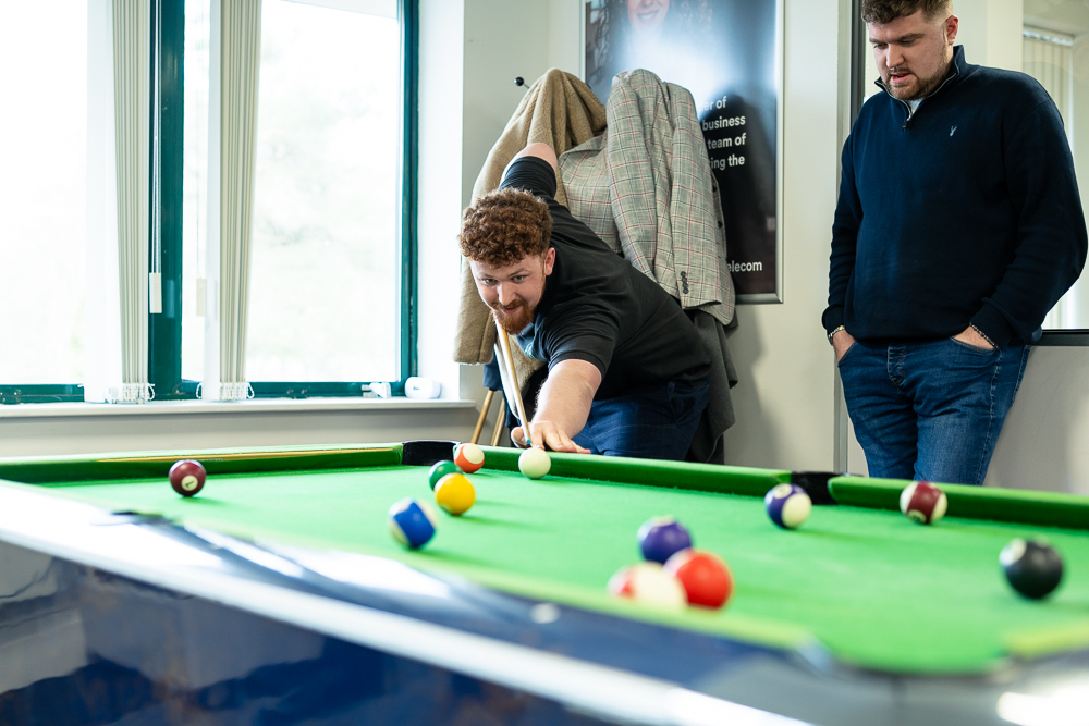 Associated Telecom team playing pool in an office break area.