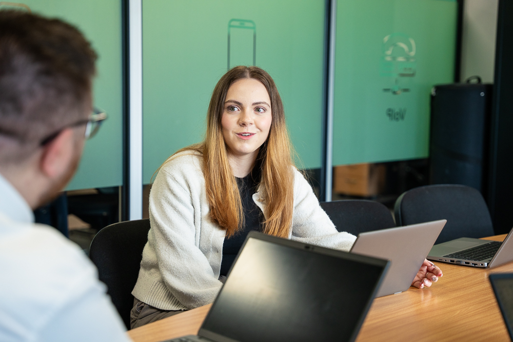 Woman working on talking to a team member in a telecom office.