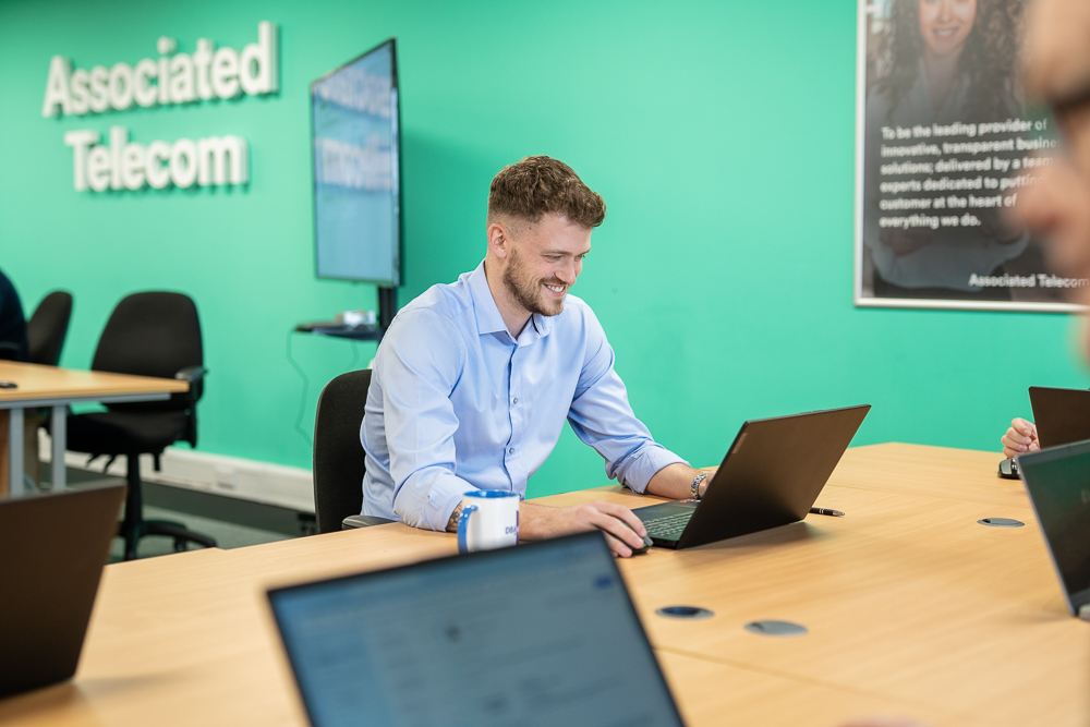 Associated Telecom employee using a laptop with office branding in the background.